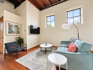 A living room with a sofa, a chair, a coffee table, and a TV mounted on the wall. - Sleepover | Superior 2BD/1BA Condo - Downtown SGF (Springfield)