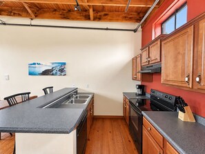 A kitchen with a central island, wooden cabinets, and a red accent wall. - Sleepover | Superior 2BD/1BA Condo - Downtown SGF (Springfield)