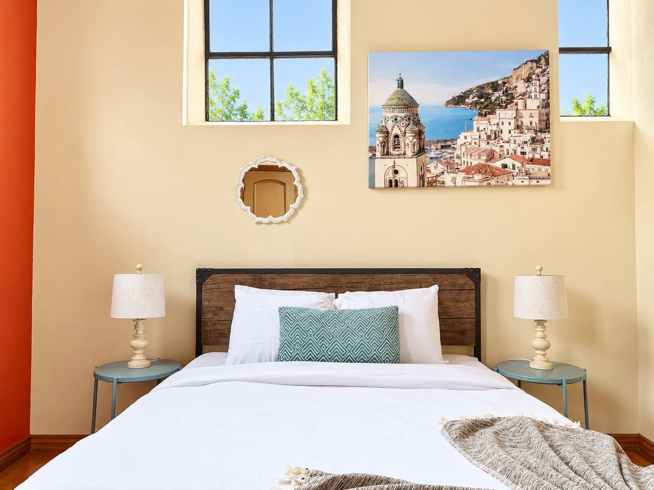 A hotel room with a bed, two bedside tables with lamps, a decorative mirror, and two framed pictures on the wall.
