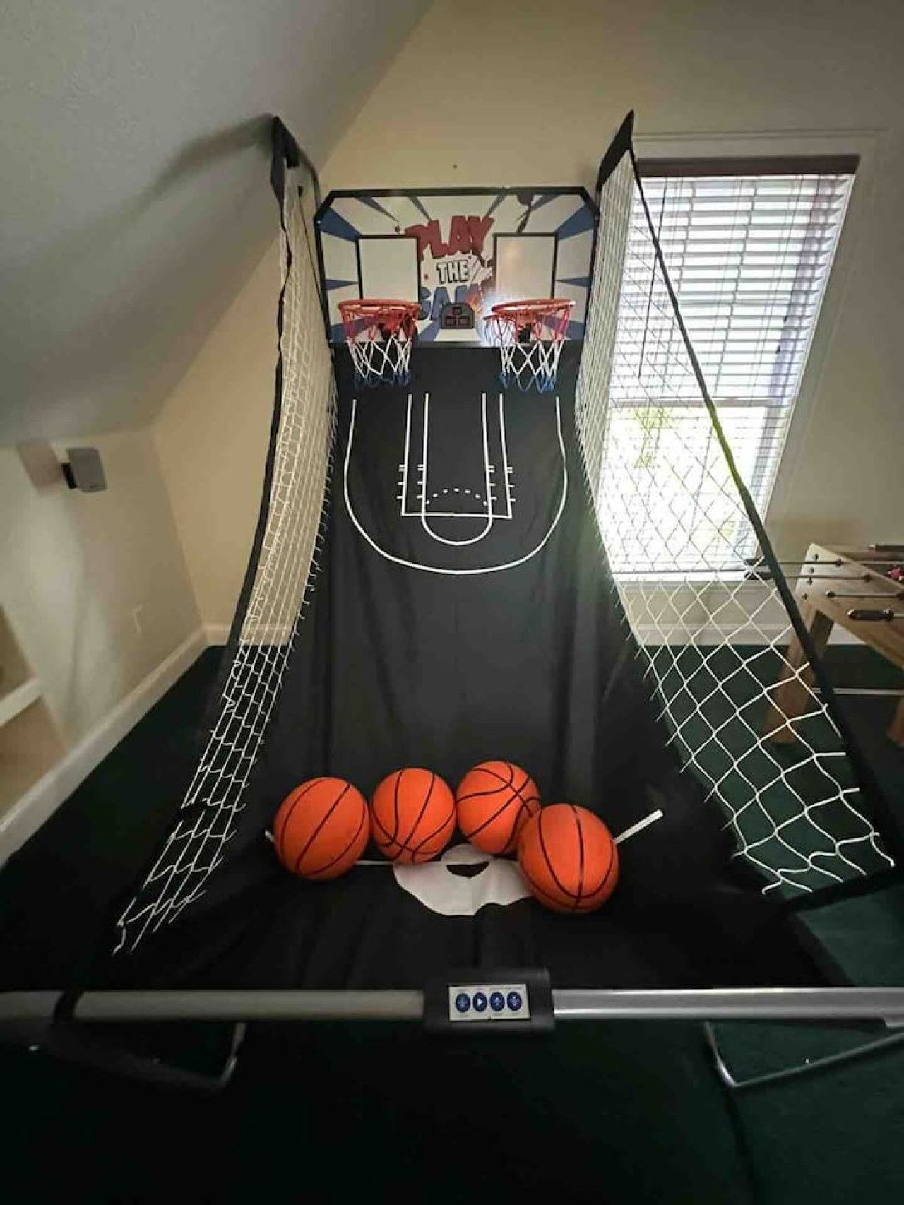 Un panier de basket avec un filet, quatre ballons de basket et un panneau de commande fixé au mur.