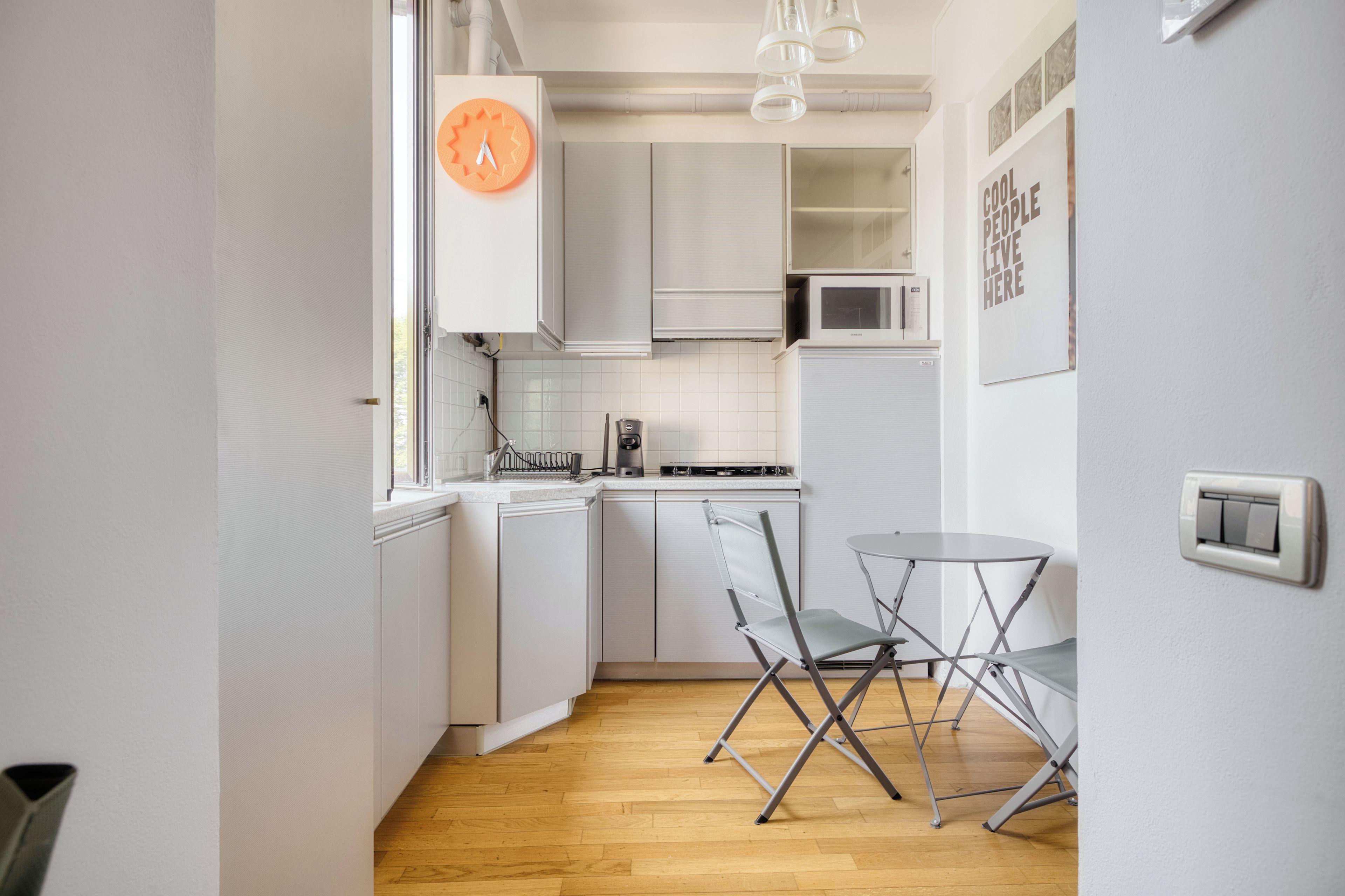 A compact kitchen with white cabinets, a microwave, a kettle, and a foldable table.