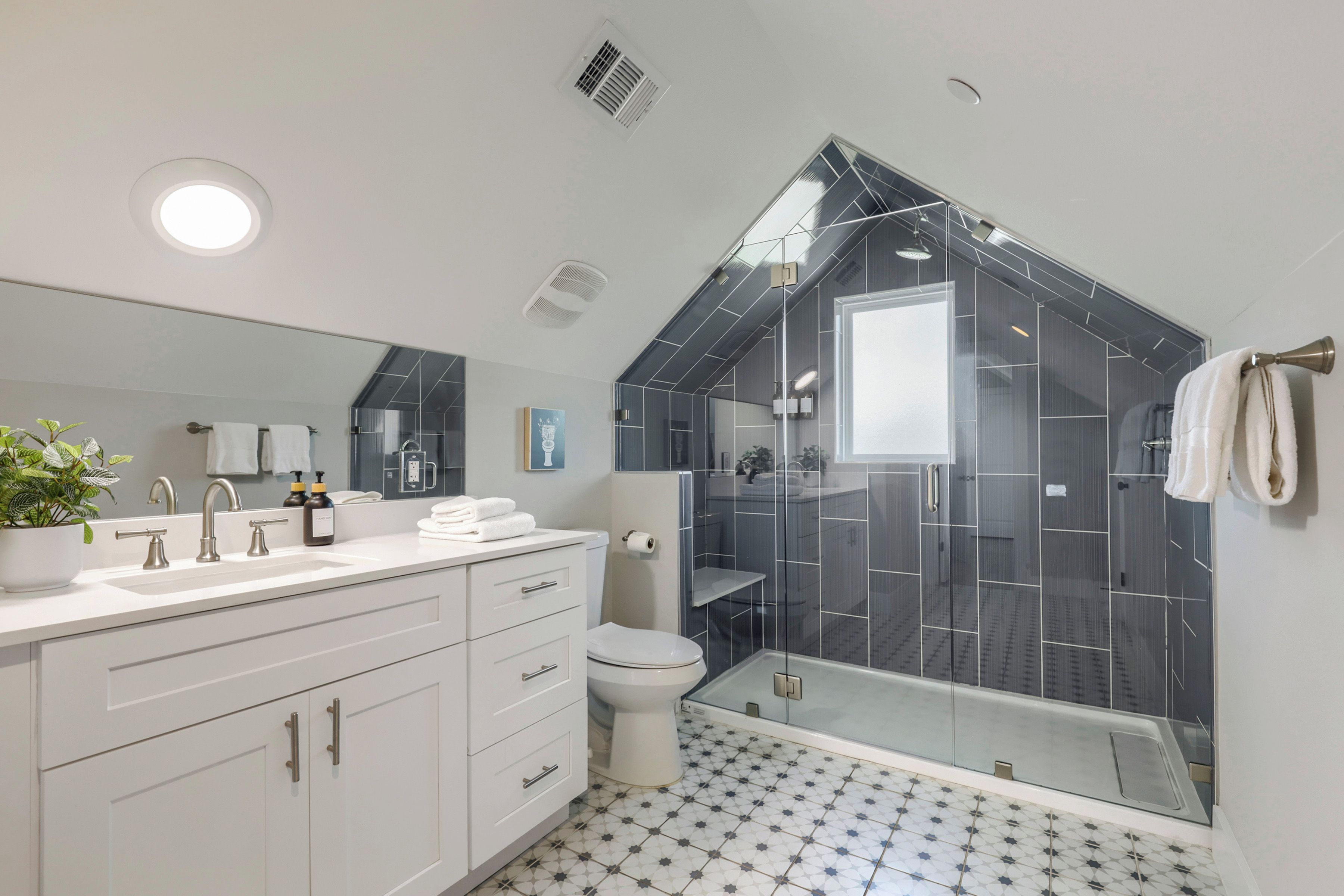 A modern bathroom with a large mirror, two sinks, a toilet, and a shower enclosure.