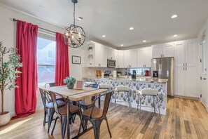 A modern kitchen with white cabinets, a stainless steel refrigerator, and a dining area with a wooden table and chairs. - Vibrant, Spacious Austin Getaway, 4BR, Sleeps 10, Near Downtown & Mueller (Austin)