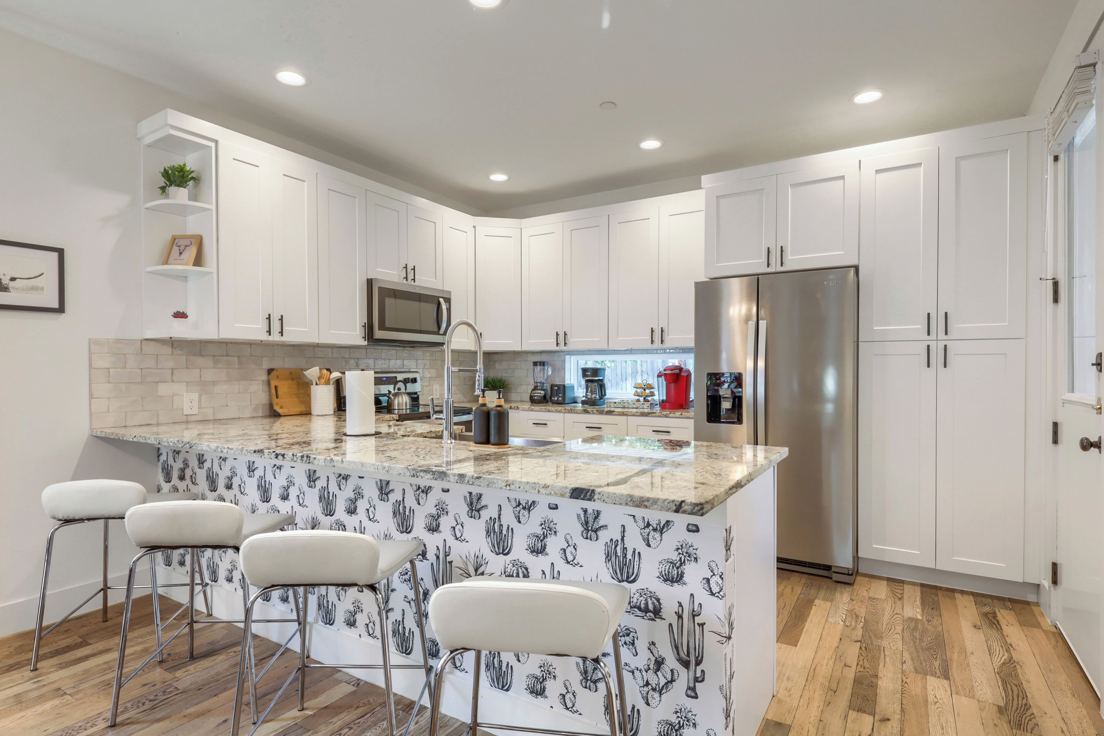 A modern kitchen with white cabinetry, a stainless steel refrigerator, and a central island with bar stools.