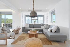 A modern living room with a grey sectional sofa, a round coffee table, and a wicker pendant light. - Le Mont Blanc | Large Group Villa Sleeps 13 Guests (Kounoupidiana)