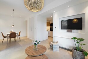 A modern living room with a dining area, a TV mounted on the wall, and a round wooden table with a vase of flowers. - Le Mont Blanc | Large Group Villa Sleeps 13 Guests (Kounoupidiana)