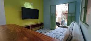 Una habitación con cama, televisor montado en la pared, mesa de madera y ventana con vista al exterior.