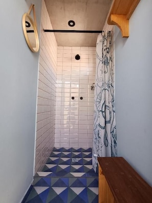 Un espacio de ducha estrecho con paredes de azulejos blancos y piso con diseño geométrico.