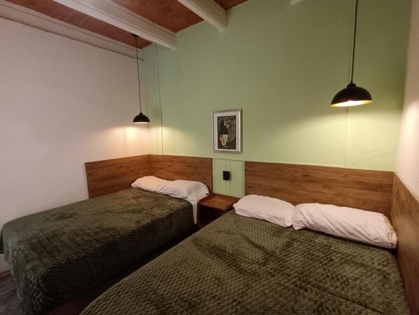 A room with two beds, wooden headboards, a framed picture on the wall, and pendant lights.