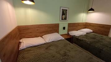Quarto com duas camas, cada uma com travesseiro e cobertor. Há um quadro na parede.