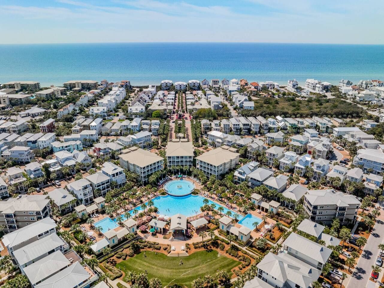 A resort with a central pool, multiple buildings, and a view of the ocean.