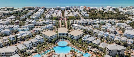 A resort with a central pool, multiple buildings, and a view of the ocean.