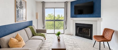 A living room with a sofa, a coffee table, a TV mounted on the wall, and a fireplace.