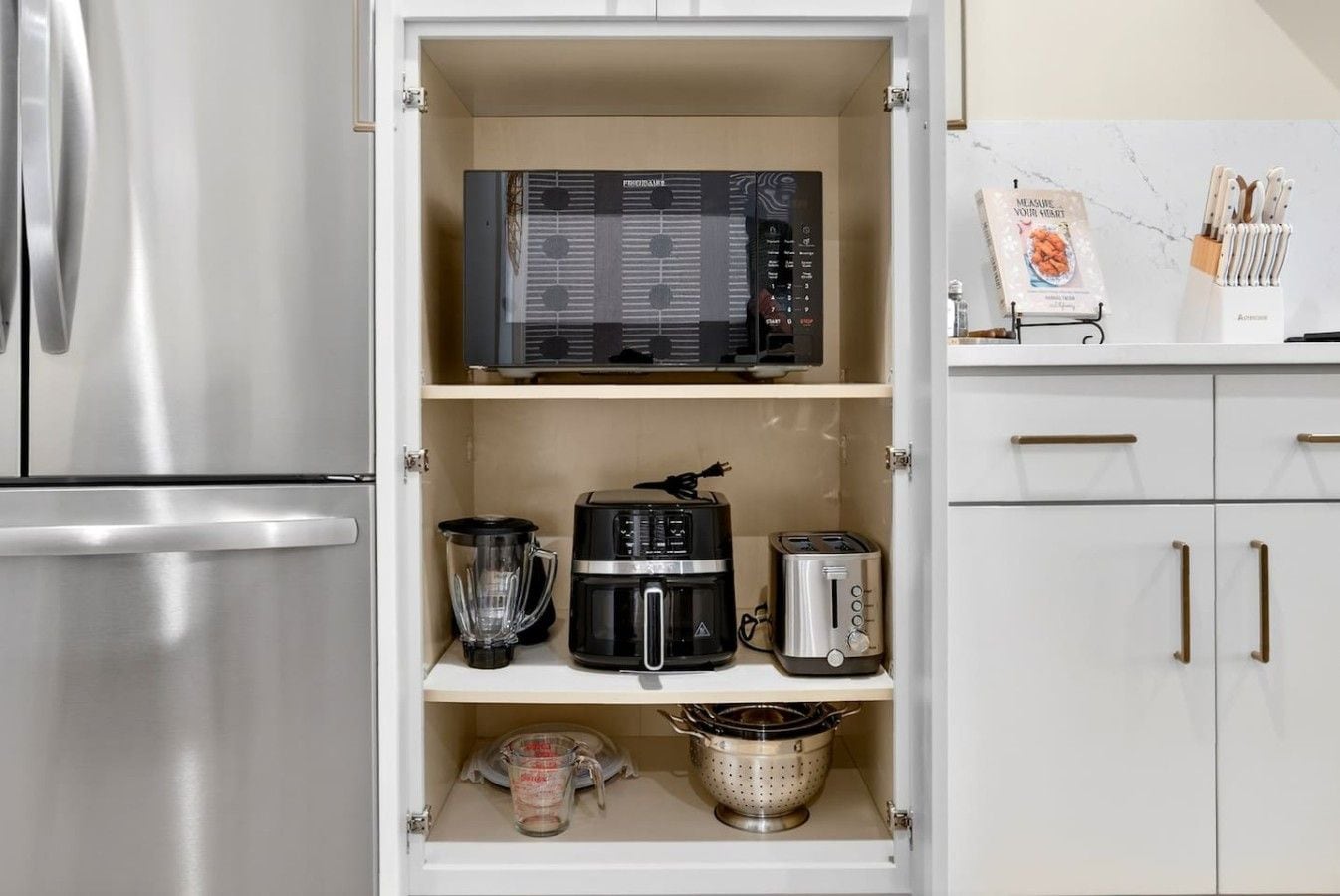 Een keuken met een ingebouwde magnetron, koffiezetapparaat, broodrooster en een vergiet op het aanrecht.