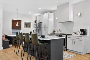Een moderne keuken met een centraal eiland, barkrukken en een eethoek met een bank.