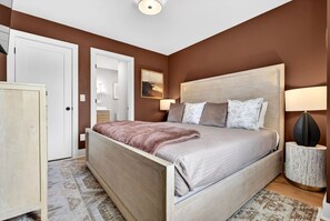 Een slaapkamer met een bed, nachtlampjes, een nachtkastje, een kledingkast en een schilderij aan de muur.