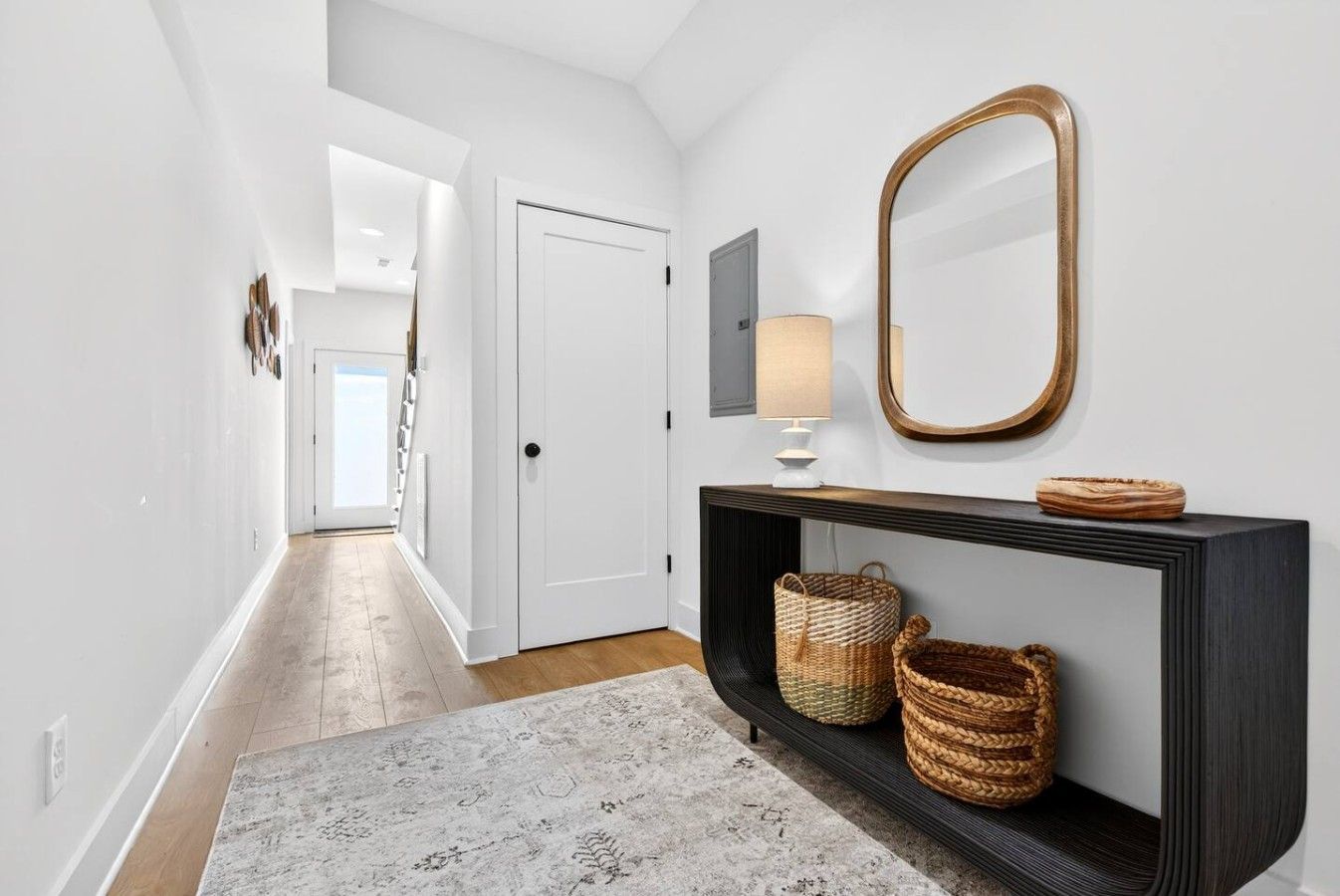 A hallway with a white door, a console table with baskets, a mirror, and a lamp.