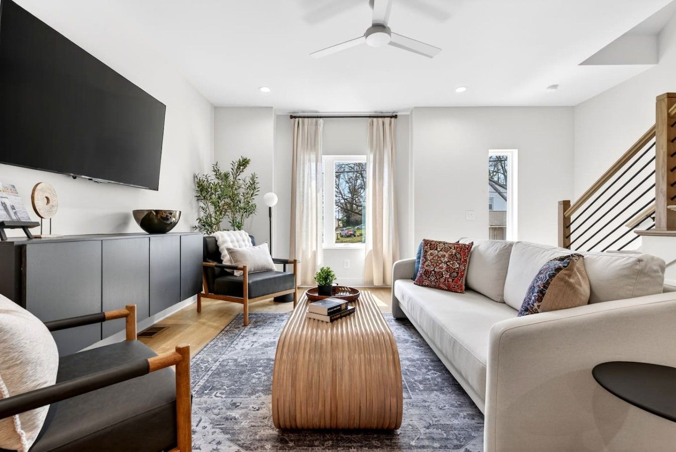 A modern living room with a flat-screen TV, a sofa, a coffee table, and a staircase.