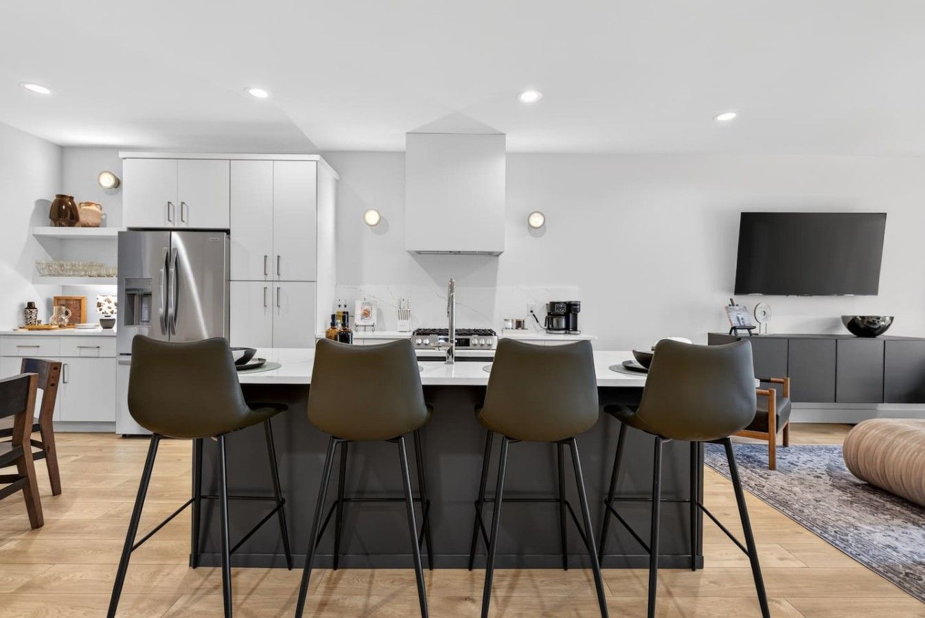 Een moderne keuken met een centraal eiland, barkrukken en een flatscreen tv aan de muur.