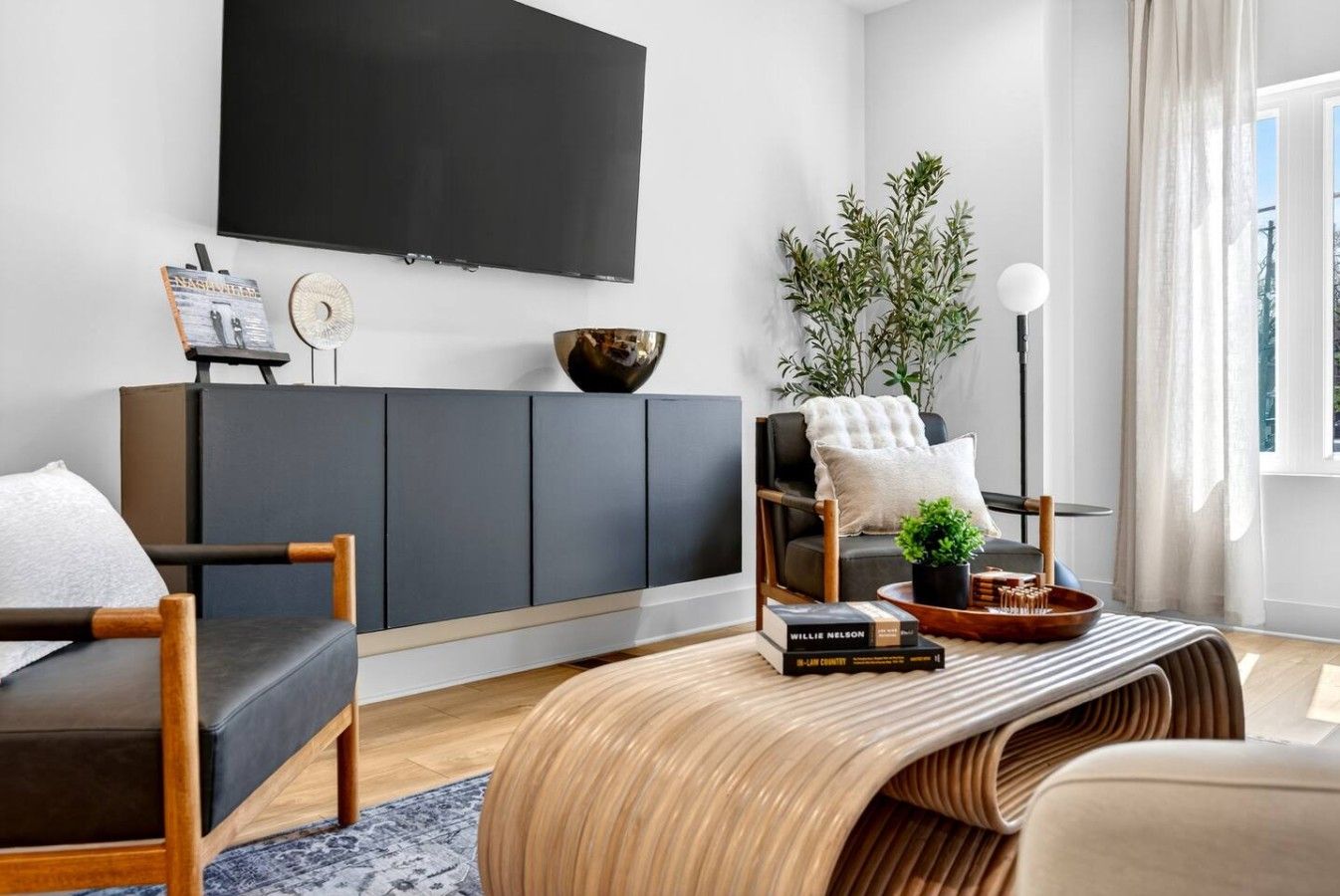 A modern living room with a flat-screen TV, a grey sofa, a wooden coffee table, and a potted plant.