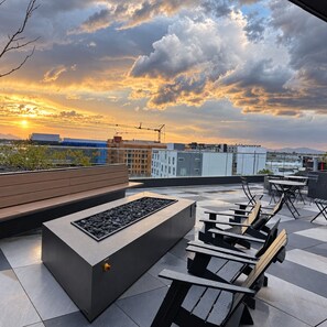 Eine Dachterrasse mit Feuerstelle, Sitzgelegenheiten und Blick auf die untergehende Stadtlandschaft.
