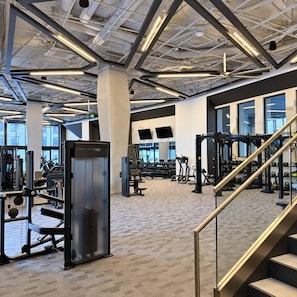 A gym with various exercise equipment, a staircase, and large windows allowing natural light. - Downtown SLC Studio | King Bed + Free Parking (Salt Lake City)