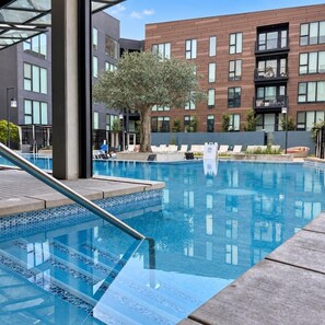 Una piscina con borde de cristal, sillas de descanso y un edificio con varias ventanas al fondo.