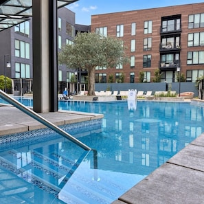 Una piscina amb taronja de vidre, gandules i un edifici amb diverses finestres al fons.