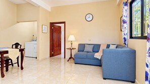 A living room with a blue sofa, a wooden table, a lamp, and a clock on the wall. - Cozy Dangriga Coastal Getaway with AC, In-Unit Laundry & Full Kitchen (Dangriga)