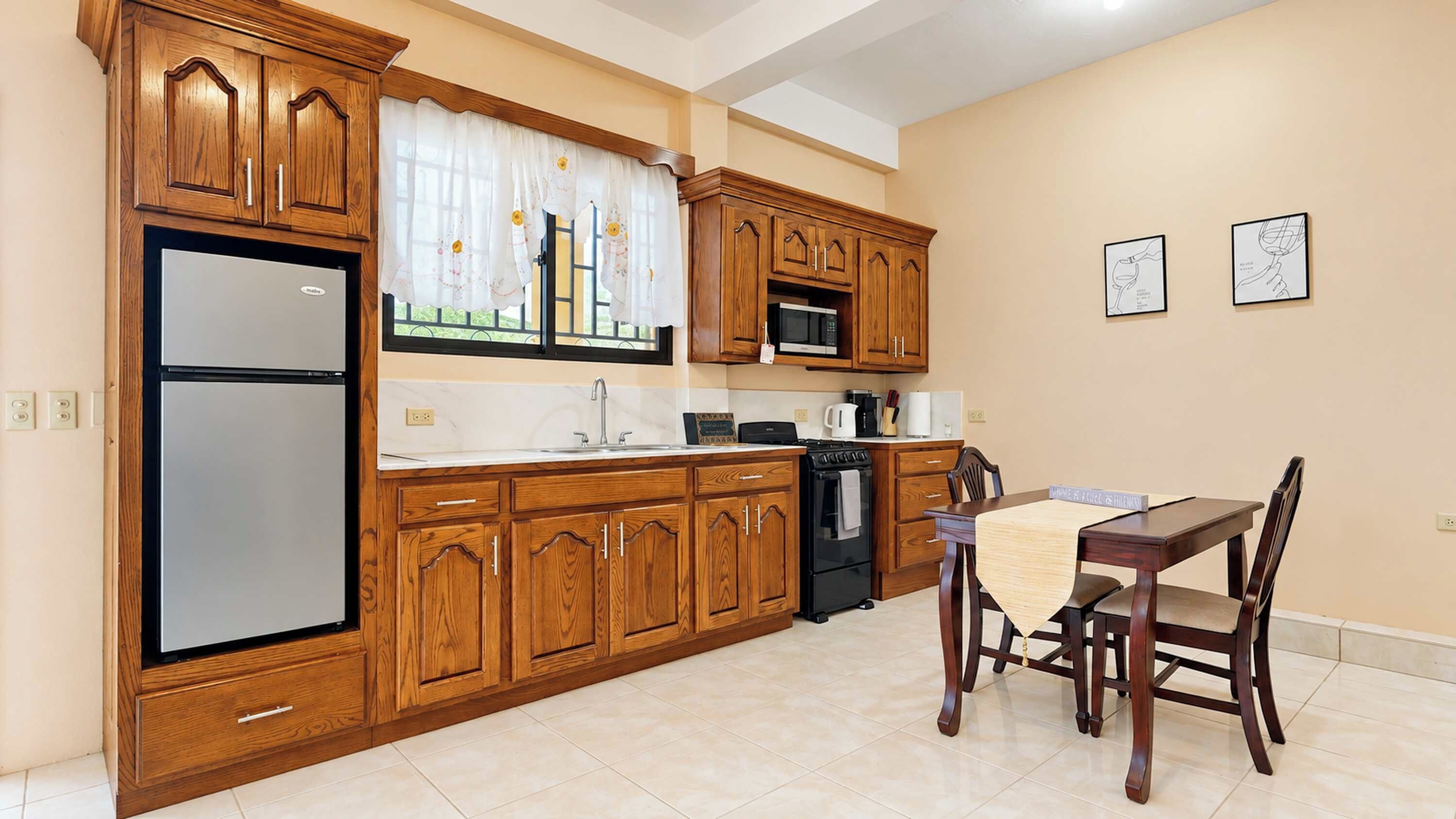 Una cocina con armarios de madera, un refrigerador, un microondas y una mesa de comedor con sillas.