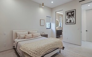 Un dormitorio moderno con una cama grande, mesitas de noche, un espejo y un cuadro en la pared.