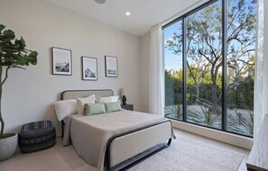 A bedroom with a large window, a bed, a bedside table, and a potted plant. - Casa Priscilla by Oraklus (Los Angeles)