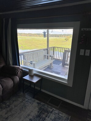 A room with a large window overlooking a deck area. There is a wooden bench and a small table with a lamp on the deck. - Cozy 2-bedroom house on Caddo lake in pleasant Mooringsport with AC (Mooringsport)
