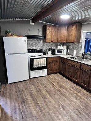 A kitchen with a refrigerator, stove, microwave, wooden cabinets, and a tiled backsplash. - Cozy 2-bedroom house on Caddo lake in pleasant Mooringsport with AC (Mooringsport)