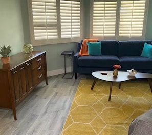 Ein Wohnzimmer mit einem dunkelblauen Sofa, einer Holzkabine, einem kleinen Beistelltisch und einem gelben Teppich mit Muster.