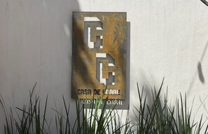 Ein Metallschild mit geometrischem Design und Text, an einer Wand befestigt, vor einem Grasbereich.