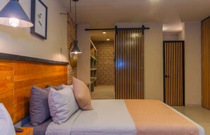 Habitació d'hotel amb un llit, una tauleta de nit, una làmpada, un armari i una porta corredissa que dona a un bany.