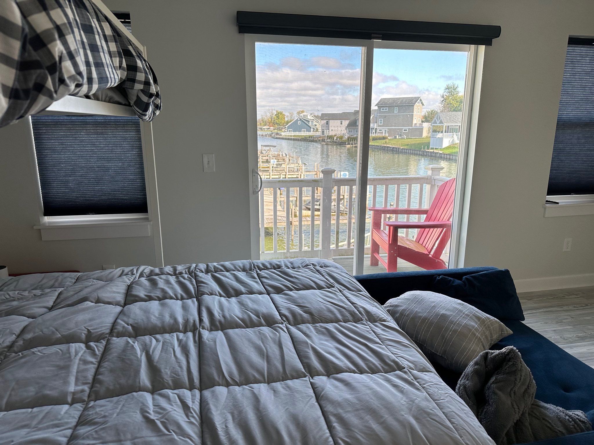 A bedroom with a large bed, a red chair, and a view of a water body and buildings through a sliding door.