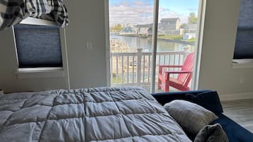 A bedroom with a large bed, a red chair, and a view of a water body and buildings through a sliding door.