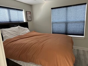 A bedroom with a bed, two windows with blinds, a headboard, and a wall-mounted artwork. - Charming 3-bedroom house on Buckeye Lake right next door to winery! (Thornville)
