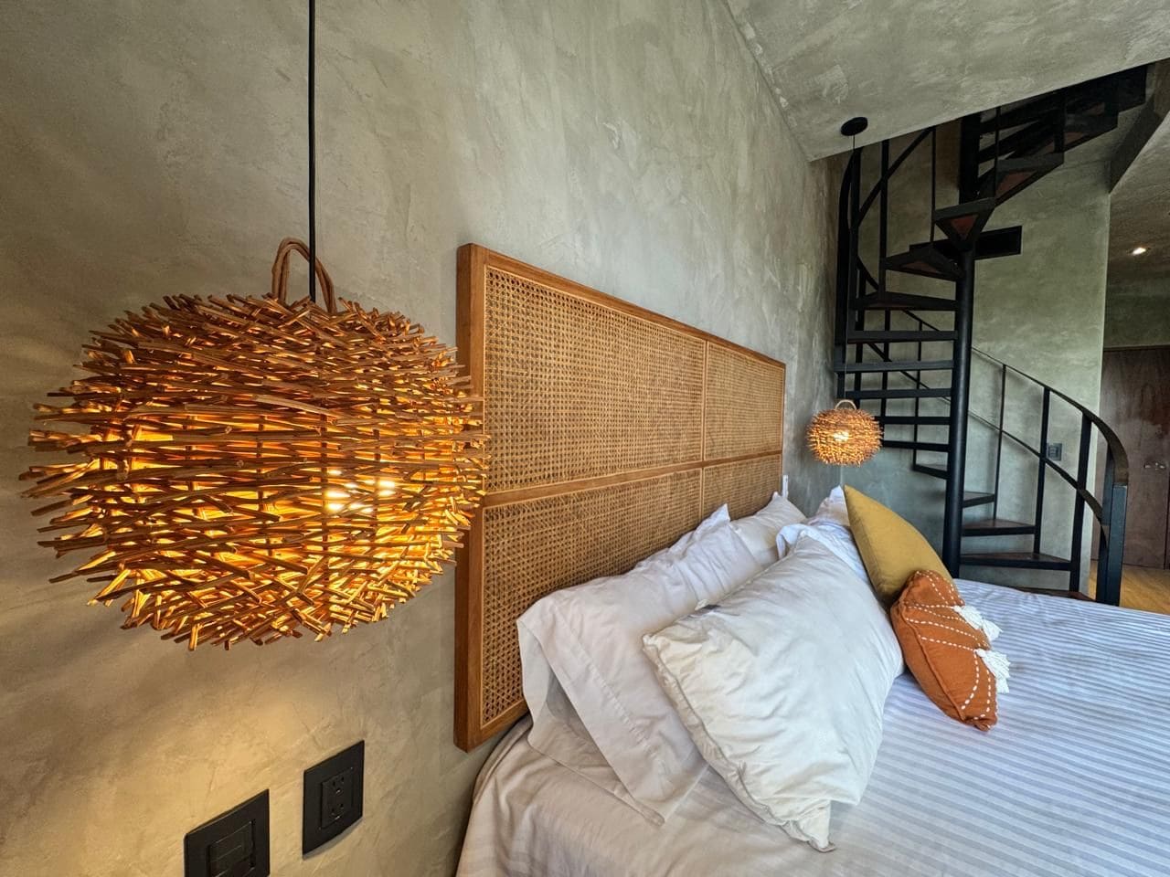 A bedroom with a bed, a headboard, a hanging light fixture, and a staircase.