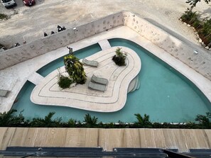 A pool with a unique shape, surrounded by a concrete deck and a wooden deck in the foreground. - TUK Tulum Tropical Escape Chic & Relaxing (Tulum)