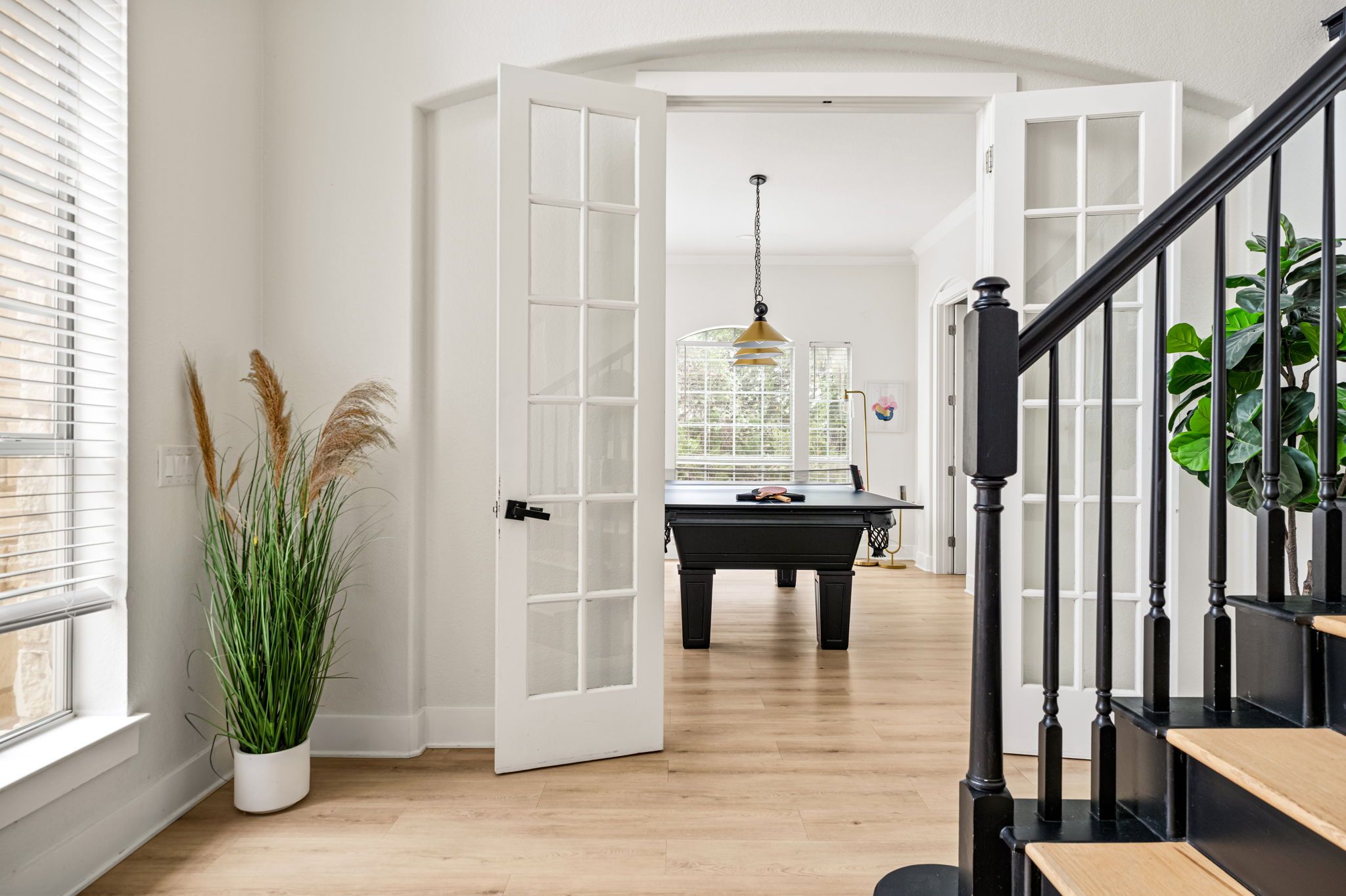 An open doorway leading to a room with a pool table, a piano, and a staircase with black railings.