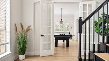 An open doorway leading to a room with a pool table, a piano, and a staircase with black railings.