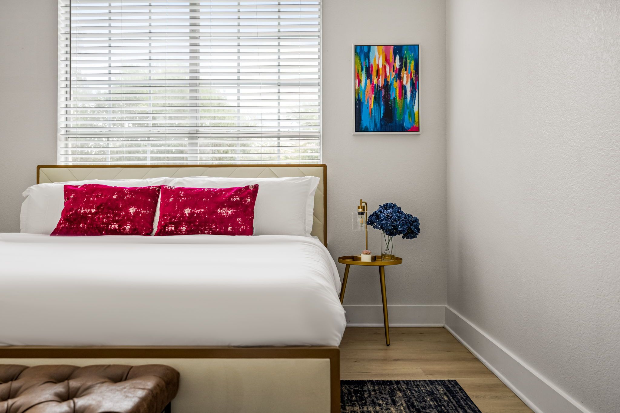 A bedroom with a bed, a nightstand with a lamp, and a painting on the wall.