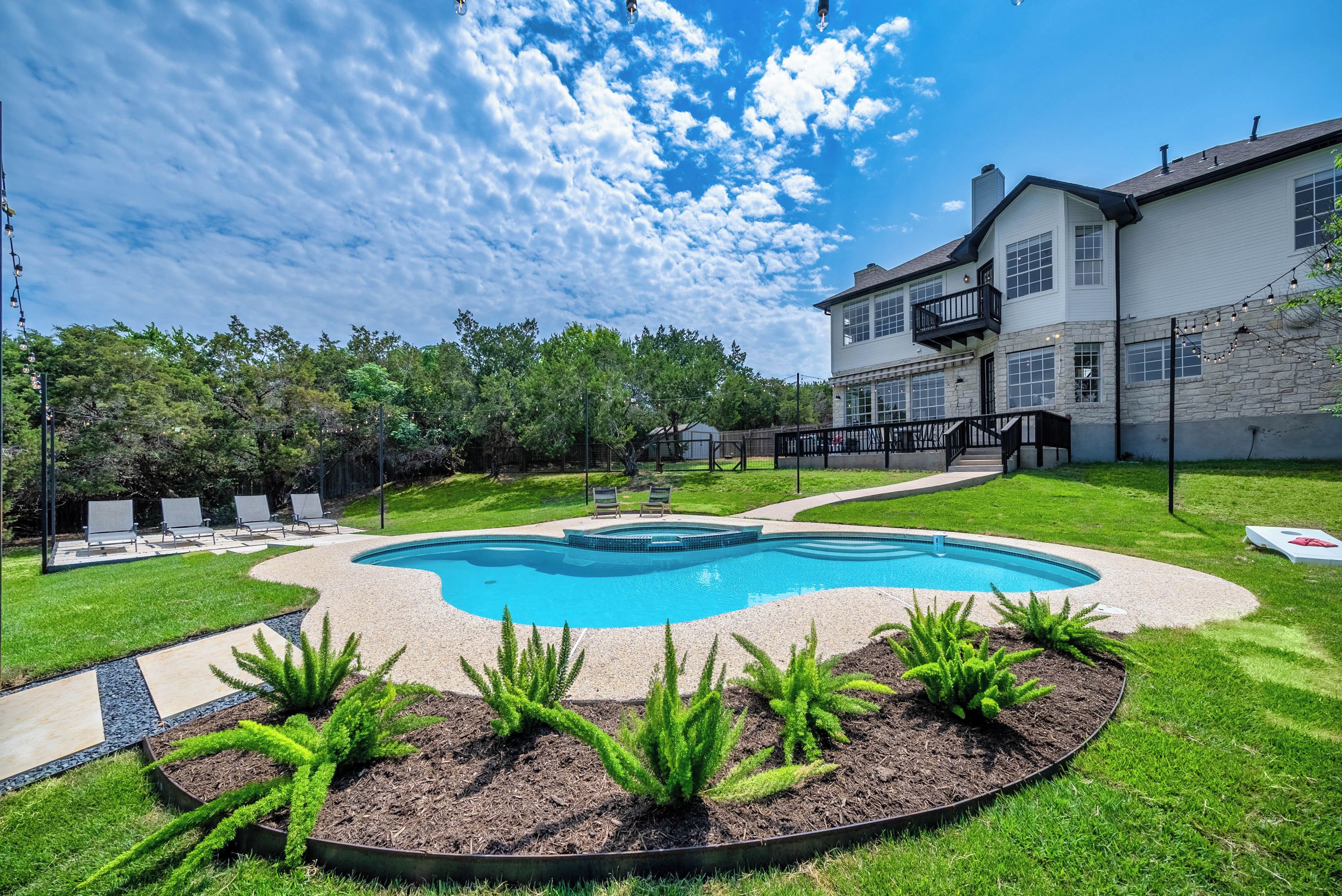 A backyard with a swimming pool, a stone wall, and a two-story house.