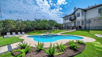A backyard with a swimming pool, a stone wall, and a two-story house.