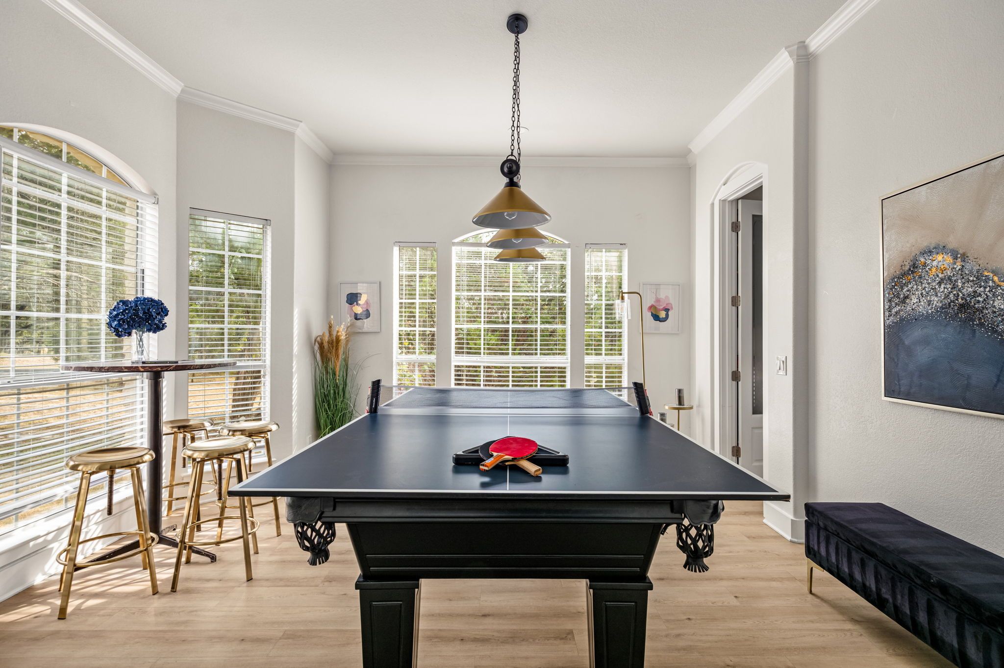 A billiards table with two cue sticks, a hanging pendant light, and a painting on the wall.