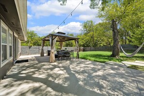 A covered patio area with a table and chairs, a hammock, and a string of lights. - NEW! Spacious SoCo Home - Big Backyard + Game Room (Austin)