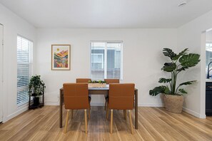 Een eethoek met een tafel en stoelen, een lijst met een kunstwerk aan de muur, en een grote potplant.